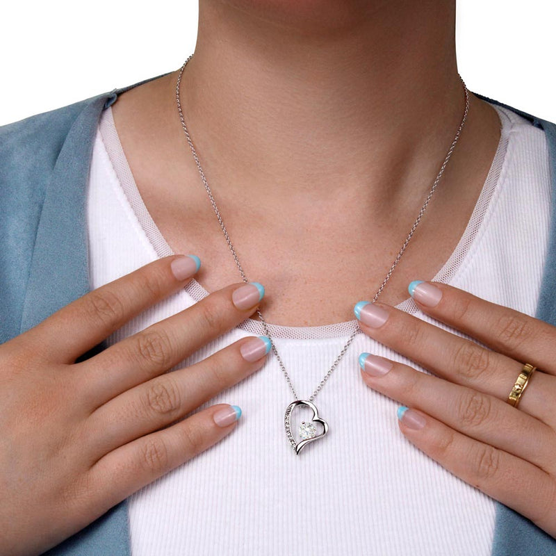 Person wearing a silver heart-shaped necklace with hands adjusting it on a white background