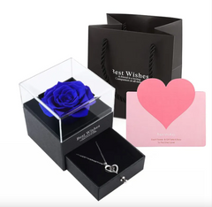 Black gift box with blue rose, heart-shaped necklace, and pink card on a white background